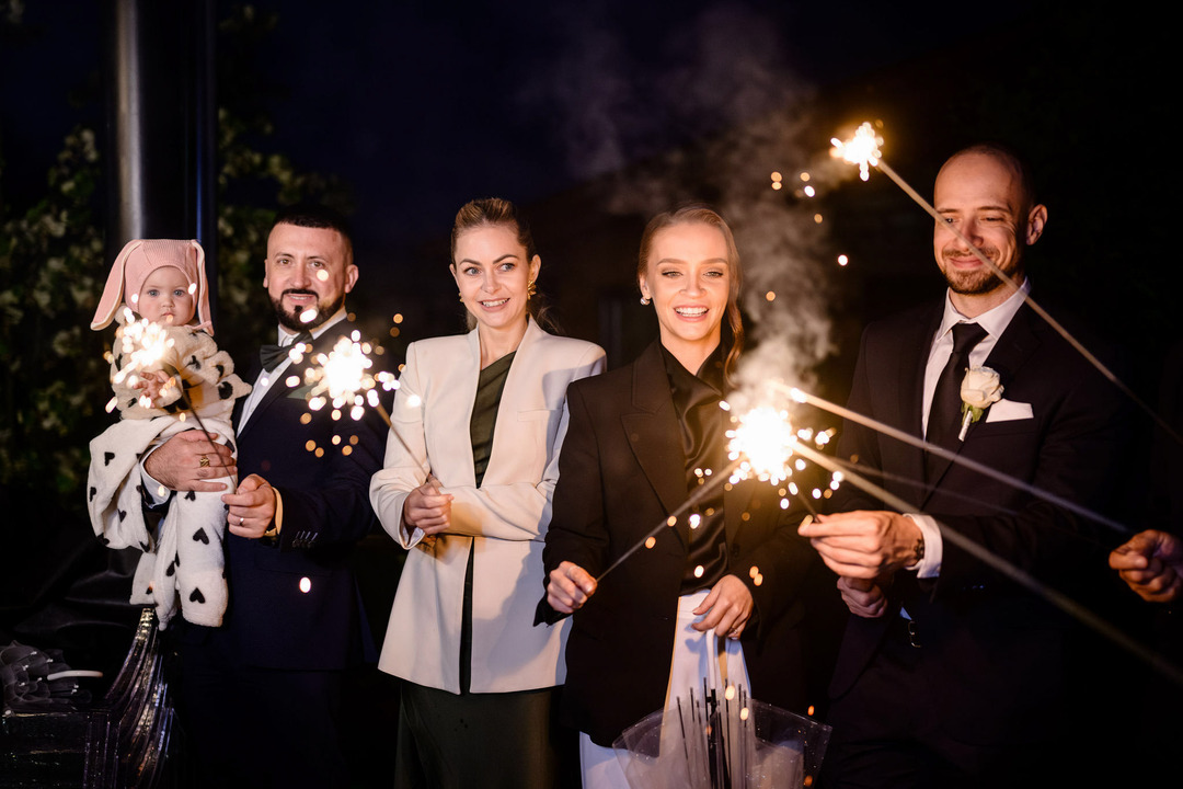 Wedding guests holding sparklers, laughing in the evening atmosphere.
