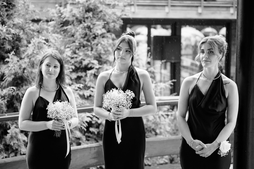 Black and white photo of three bridesmaids in black dresses holding white flowers.
