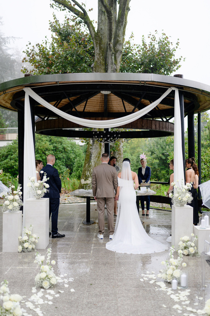 The bride and groom stand in the decorated gazebo in the garden of Villa Cattaleya, with the ground still wet from the rain.

