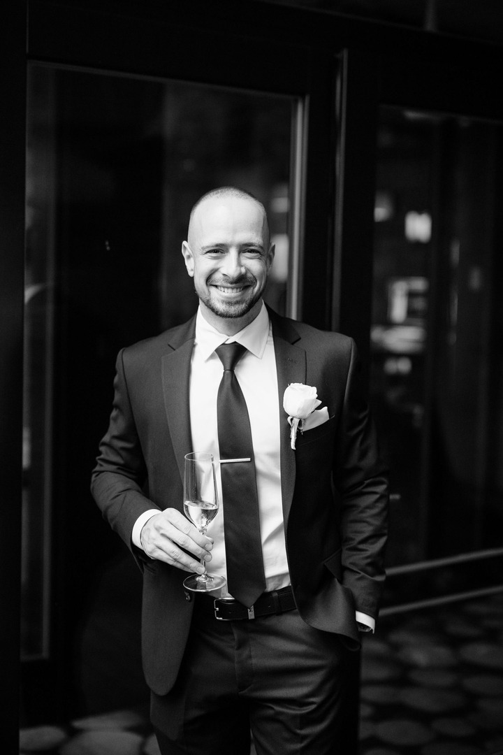 Black and white photo of the best man laughing with a glass in his hand.
