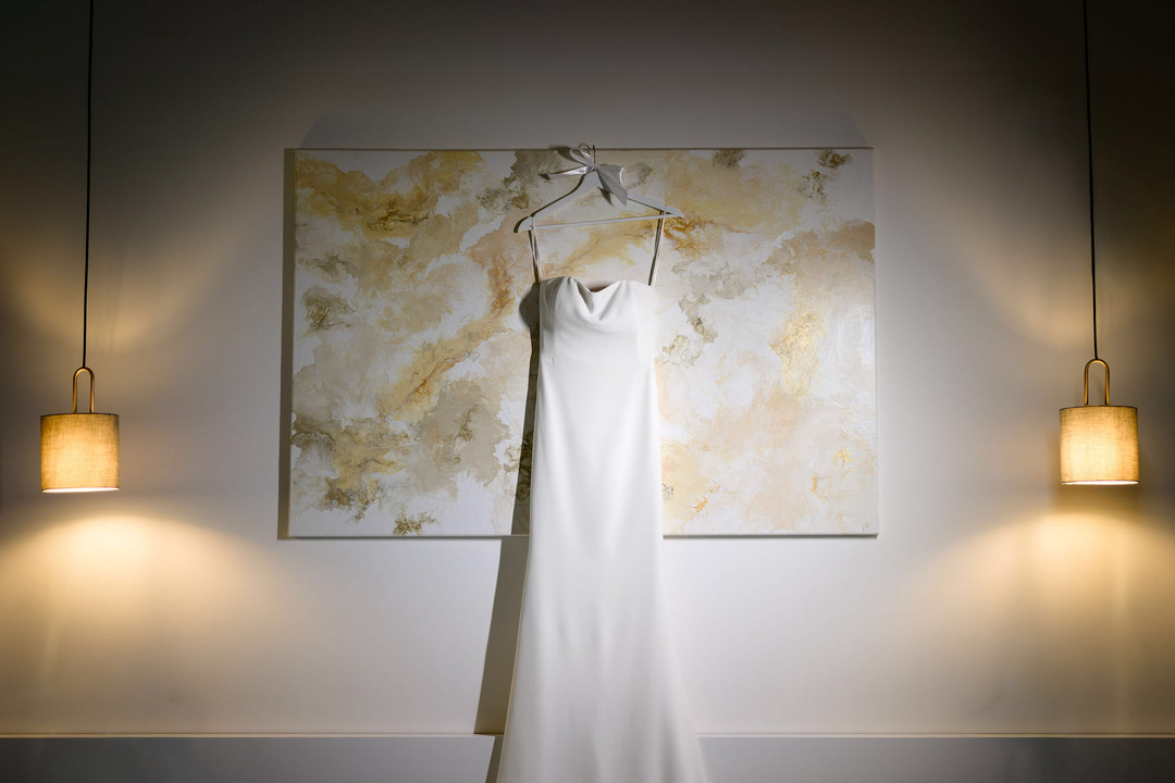 The bride's long, straight white wedding dress hangs on a large painting in a room at Villa Cattaleya.

