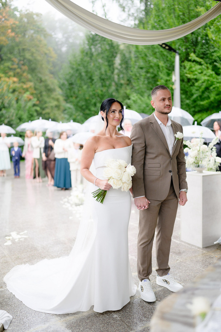 Low-angle shot of the bride and groom holding hands, looking at the officiant and smiling.
