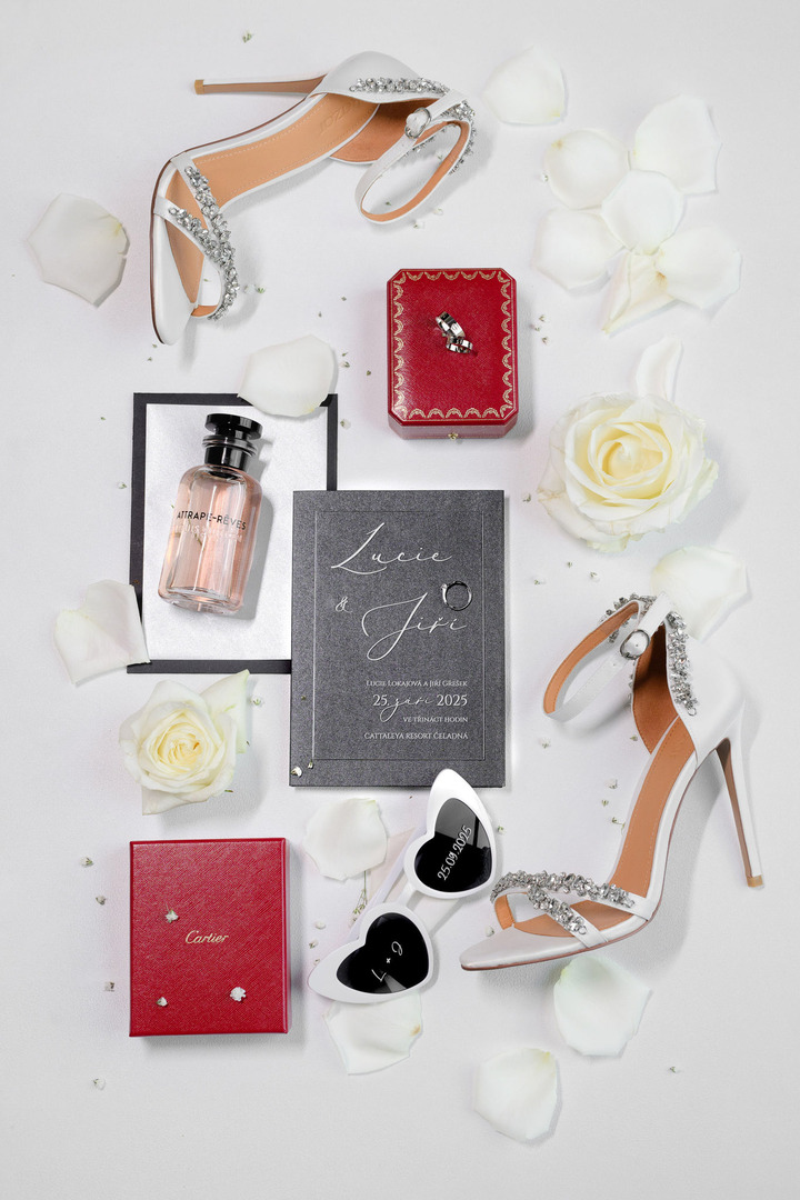 Wedding flatlay – invitations, wedding rings, flowers, bride's shoes, perfume, and heart-shaped sunglasses.
