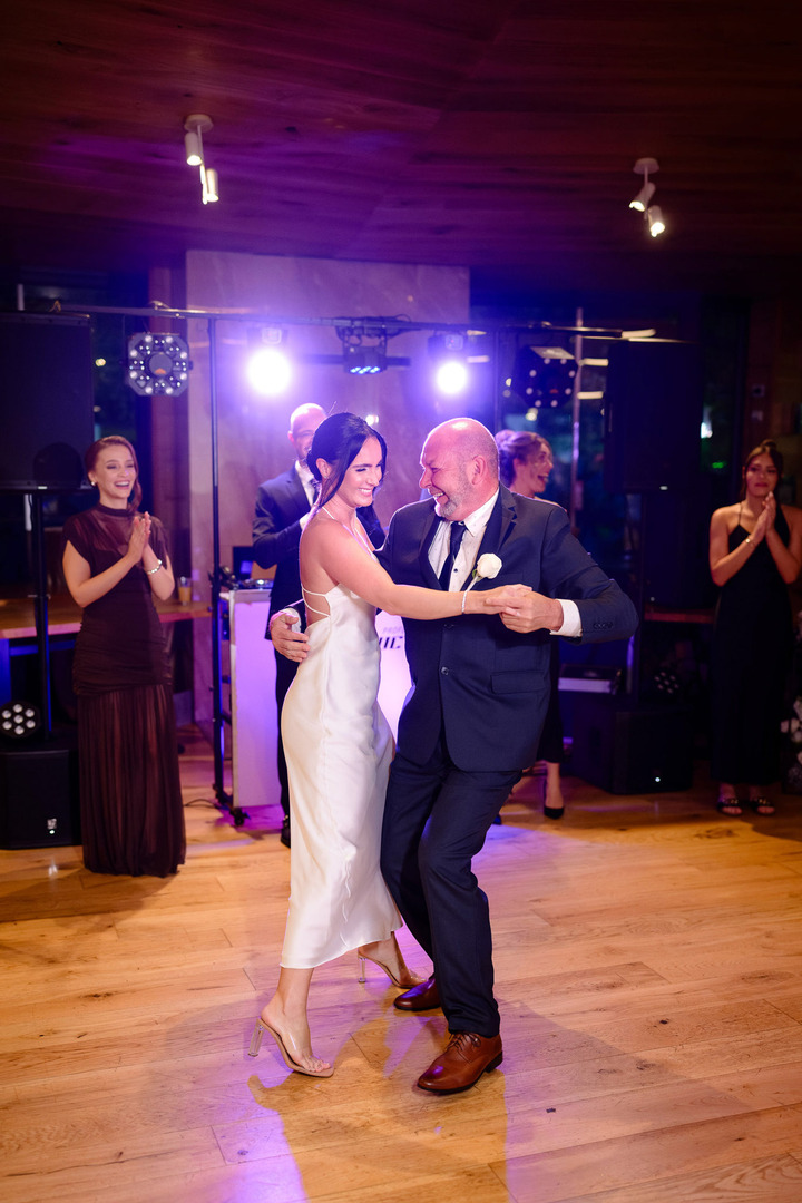 The bride happily dances with her father, illuminated by purple light.
