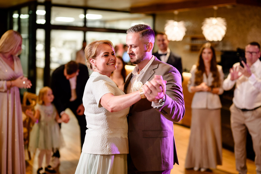 The groom dances with his mother, surrounded by supportive wedding guests.
