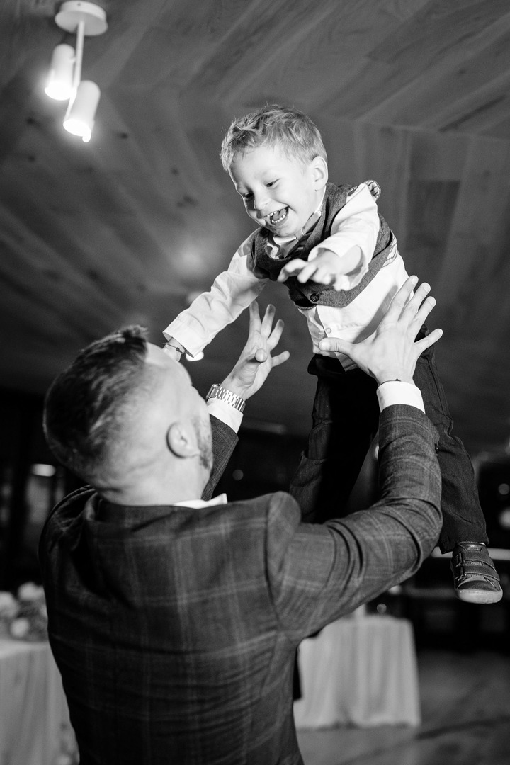 Black and white photo of a young man joyfully tossing his son into the air, the boy laughing with excitement.
