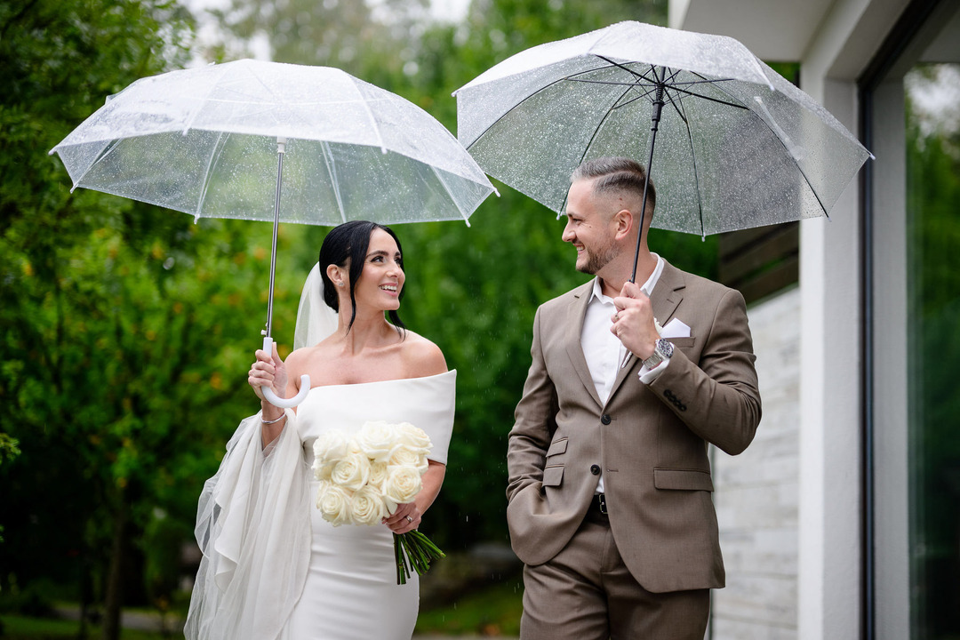 The bride and groom walk through the garden of Villa Cattaleya, holding umbrellas in their hands, laughing at each other.
