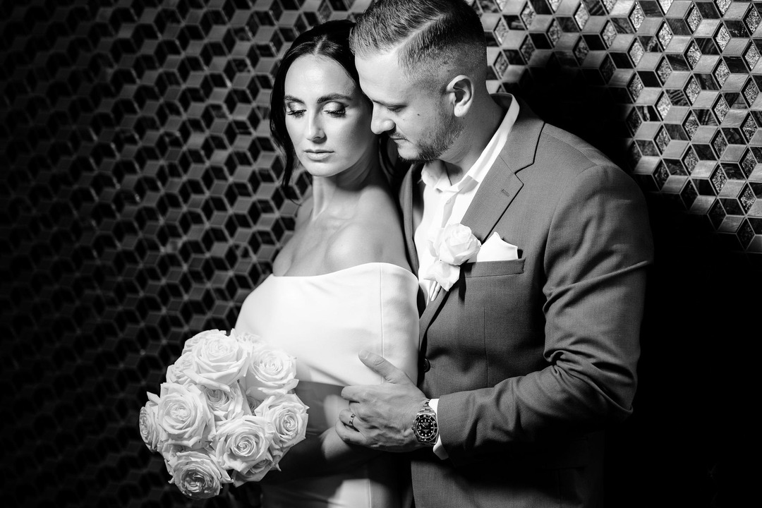 Black-and-white photo of the groom hugging the bride from behind, both with their eyes closed in this tender moment.
