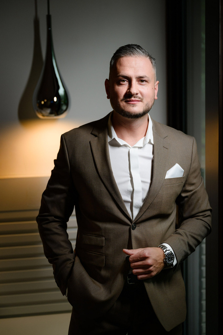 The elegant groom in a brown suit and white shirt smiling optimistically at the camera.
