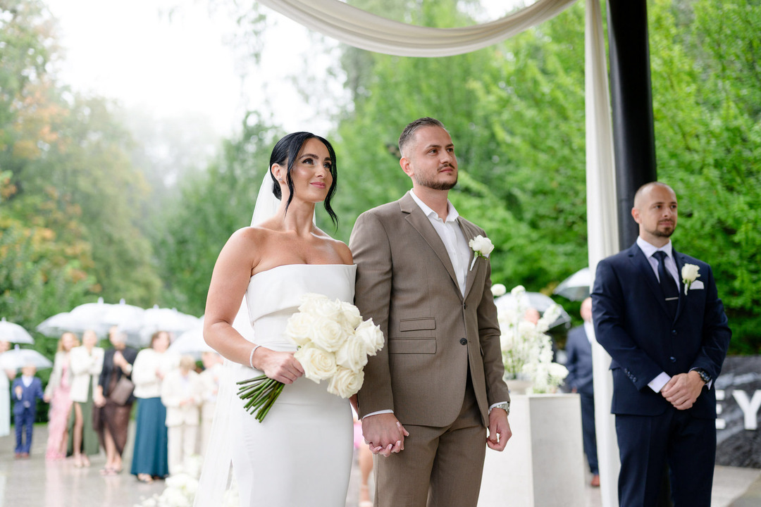 Low-angle shot of the bride and groom holding hands, looking at the officiant and smiling.
