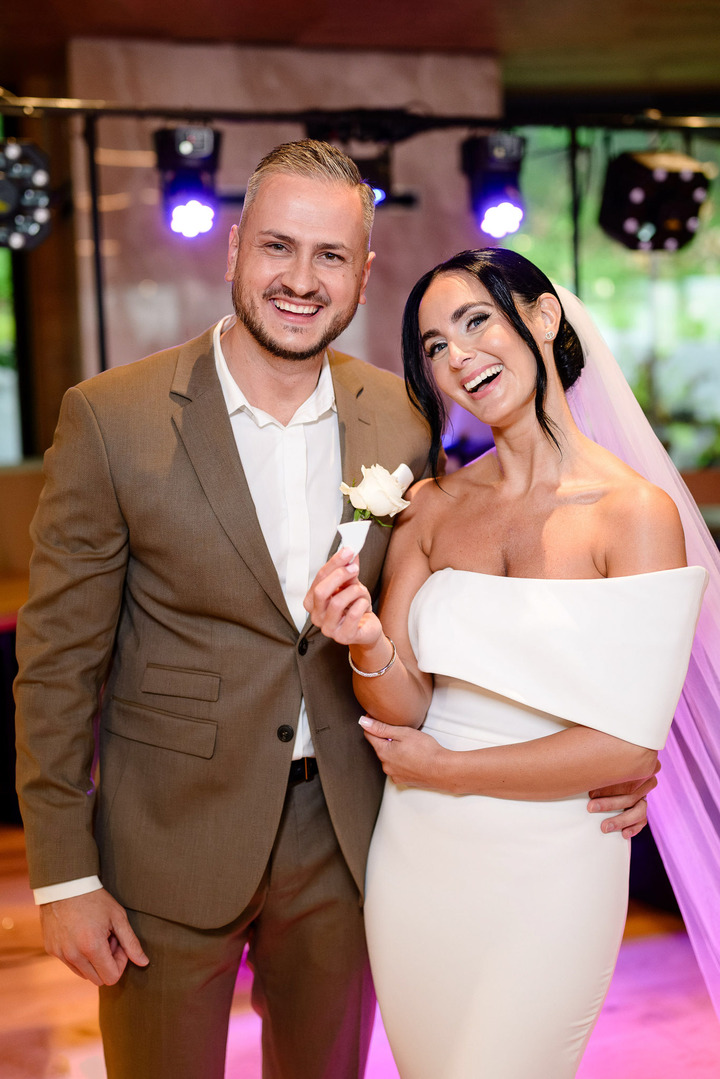 Newlyweds smiling at the camera, holding a piece of a broken plate from the wedding plate-breaking tradition.
