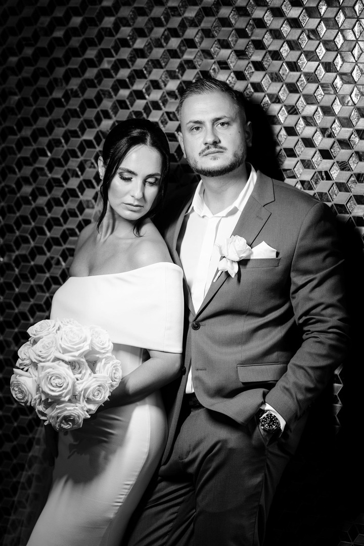 Black-and-white photo of the newlyweds, the bride leaning her back against the groom, enjoying his closeness.
