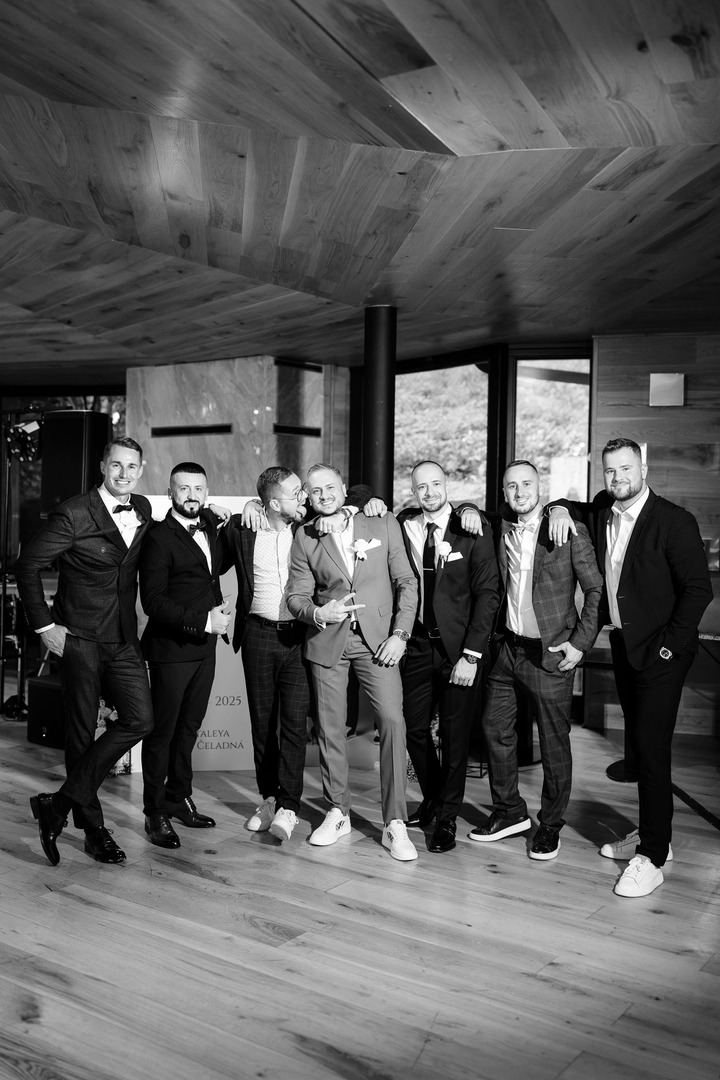 Black-and-white photo of a group of guys with the groom, laughing, teasing each other, and leaning on one another. A picture full of ease and joy.
