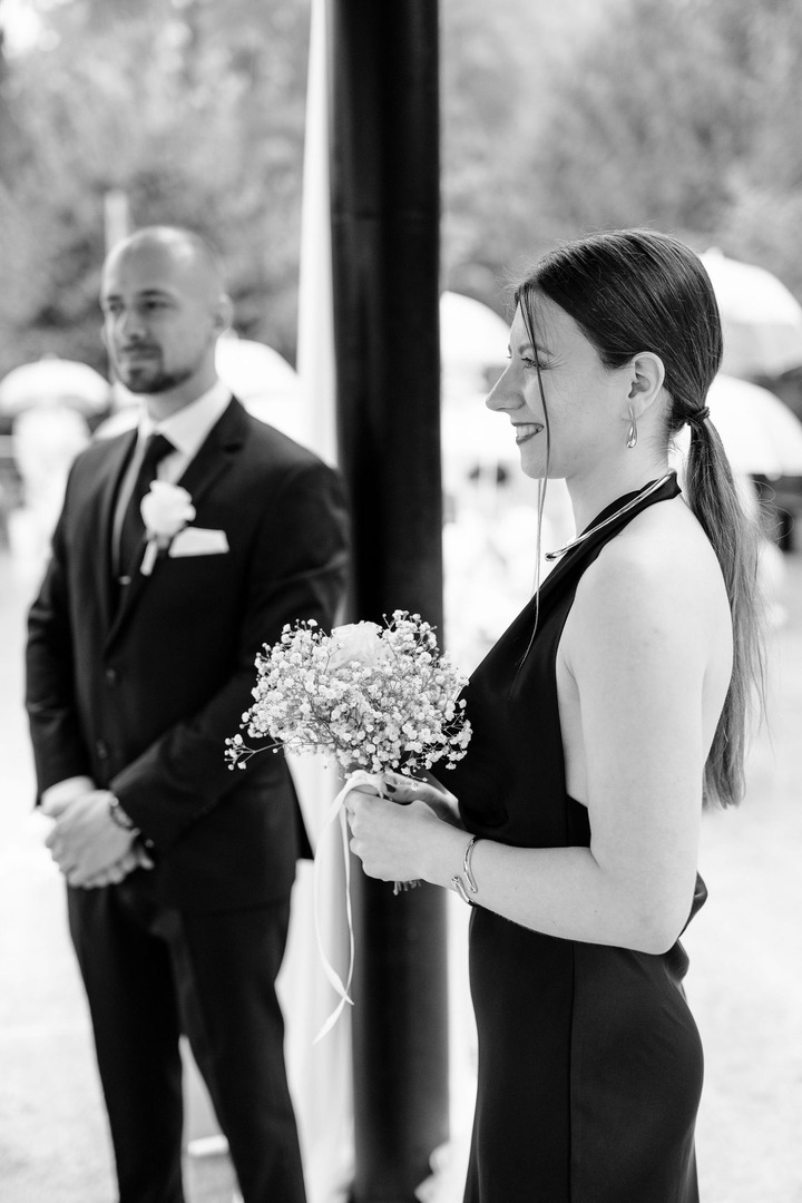 Black and white photo showing the bride’s friend standing in the foreground with the groom’s best man in the background.
