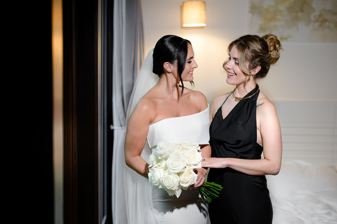 The bride is hugging her sister, and they are smiling at each other.
