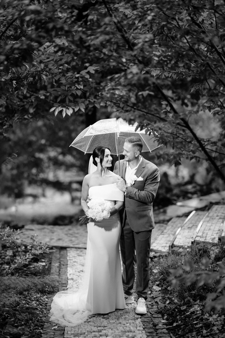 The bride and groom are standing under a single umbrella in the garden of Villa Cattaleya, smiling at each other.
