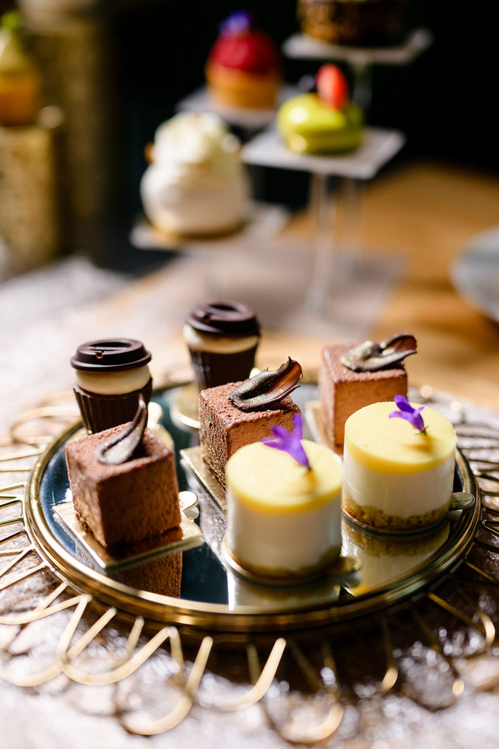 Beautiful cakes arranged on a golden plate, decorated with chocolate and violets.
